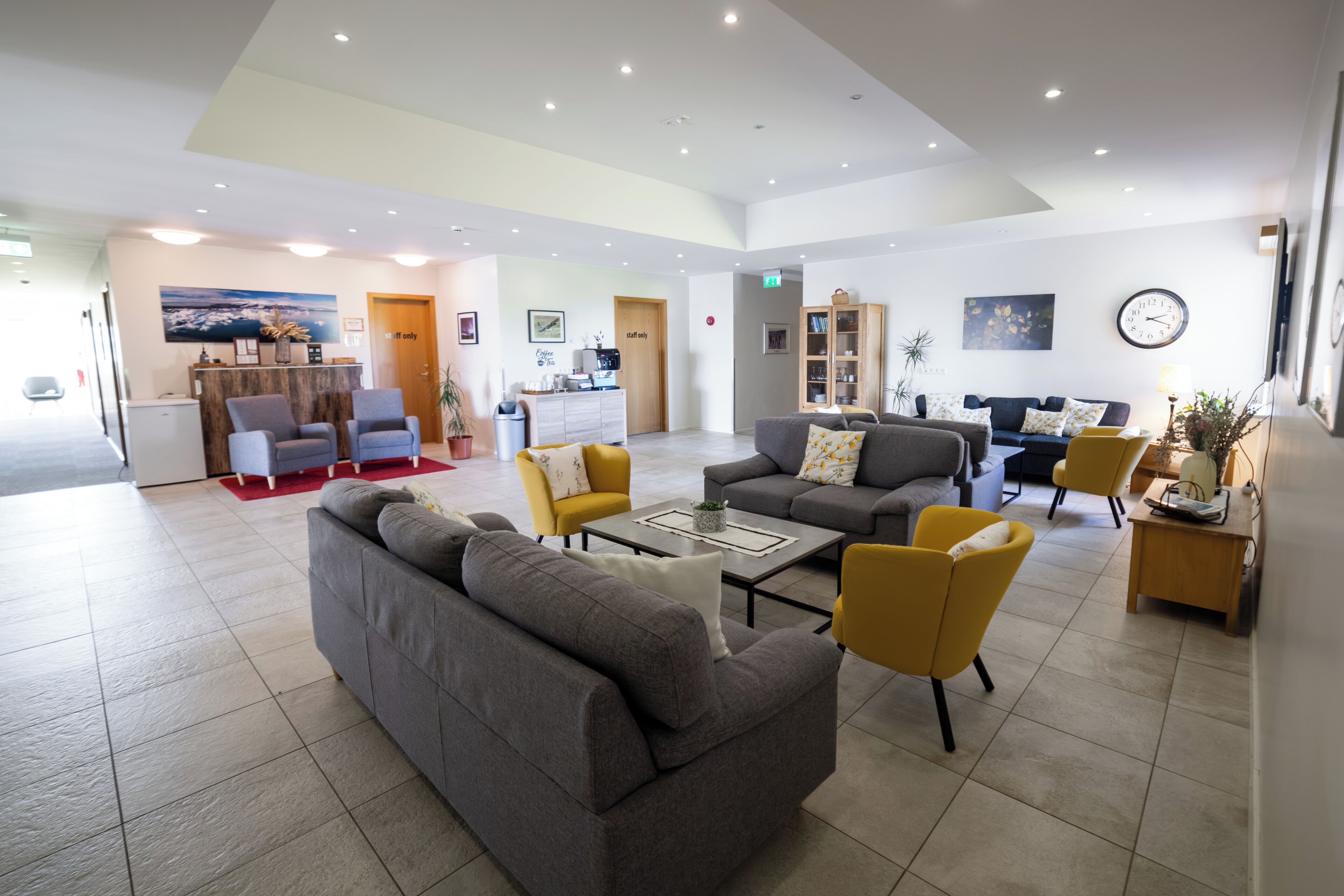 A spacious lobby with a reception desk, seating area with sofas and armchairs, and a coffee station.