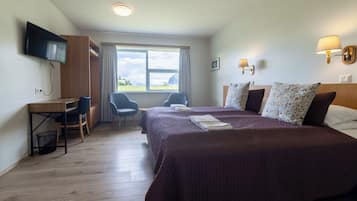 Habitación de hotel con cama, dos mesitas de noche, un escritorio, una silla, televisor y ventana con vistas.