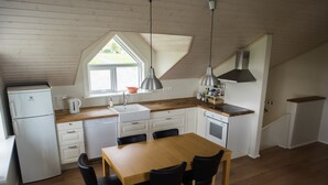 A compact kitchen with a wooden table and chairs, a white refrigerator, and a window with a view of the outdoors.