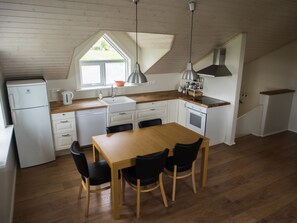 Cozinha compacta com mesa e cadeiras de madeira, geladeira branca e janela com vista para o exterior.