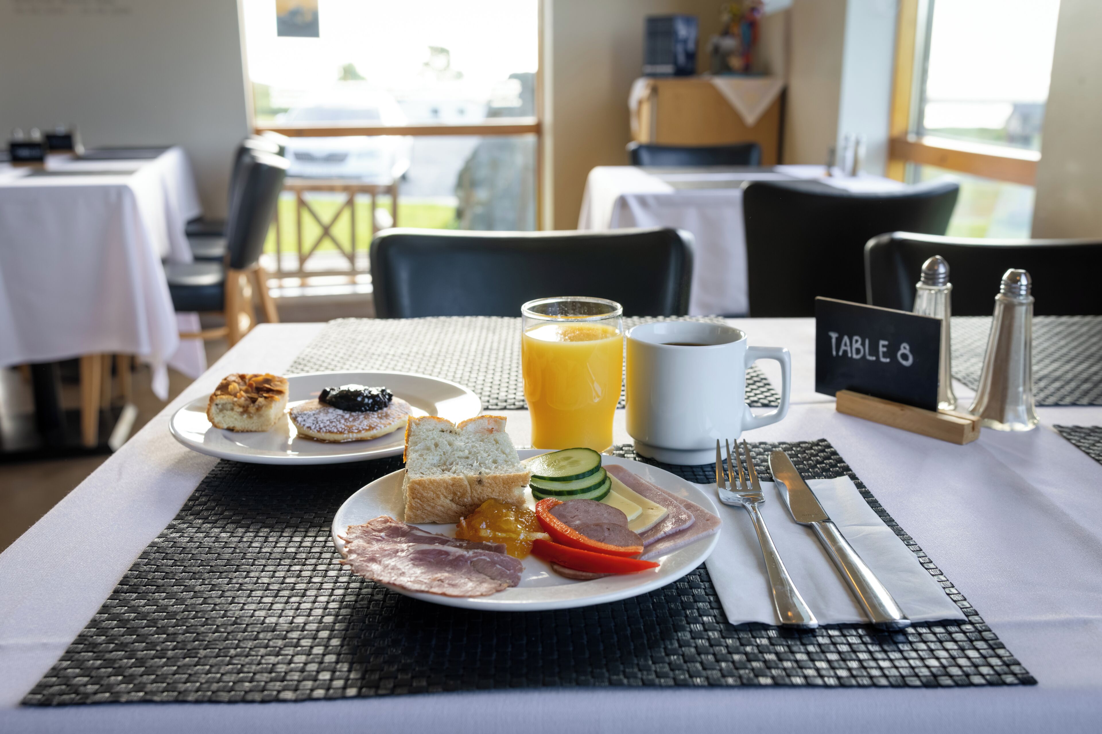 A breakfast setting with a plate of food, a cup of coffee, and a glass of orange juice on a table.