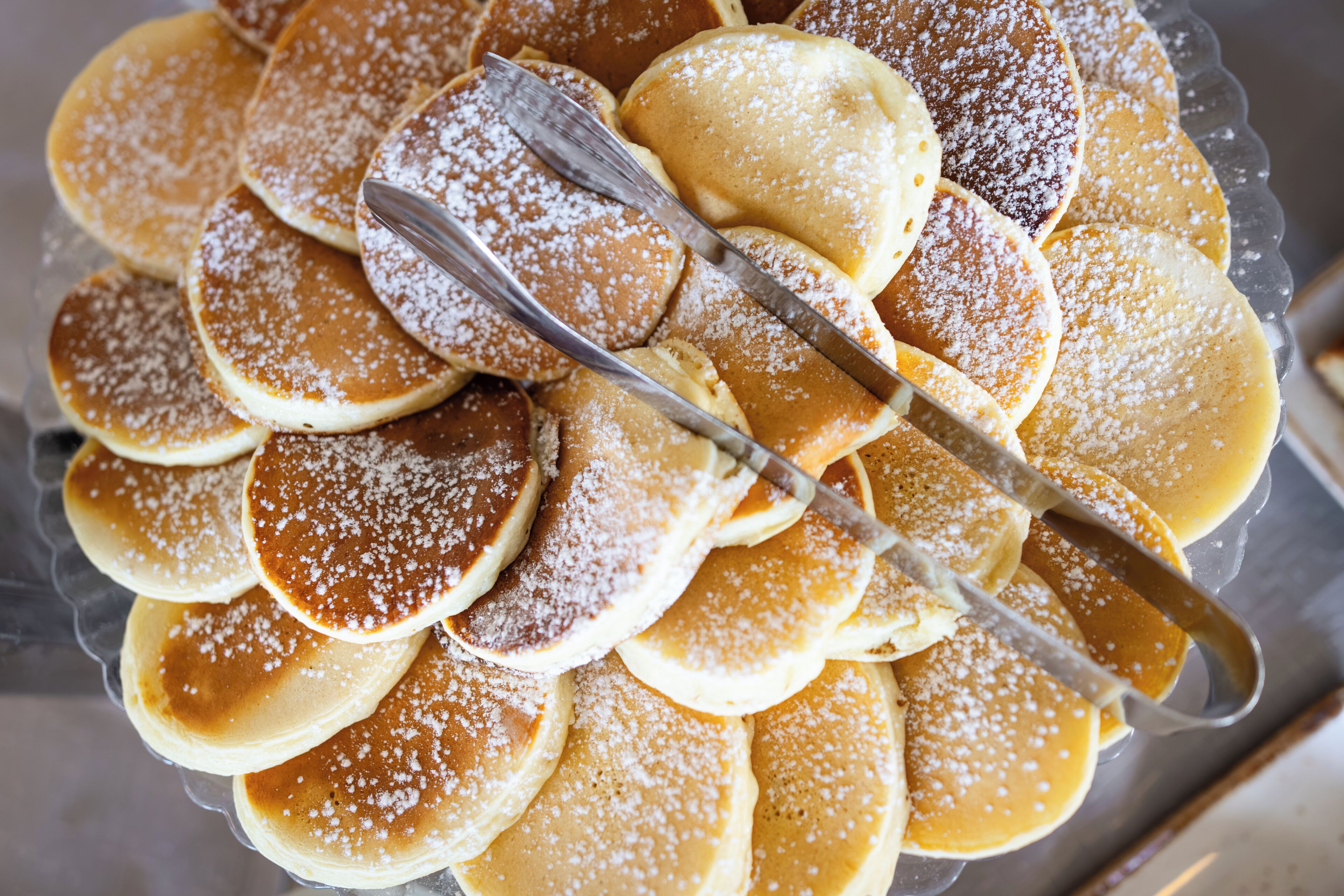 A stack of pancakes with powdered sugar on a glass plate.