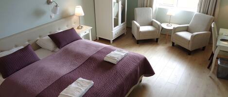 Habitación de hotel con una cama grande, dos sillones, una mesita, un armario y una ventana con cortinas.