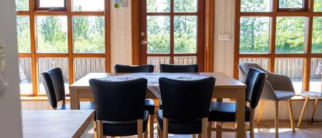 A dining area with a wooden table and chairs, large windows with a view of trees, and a thermostat on the wall.