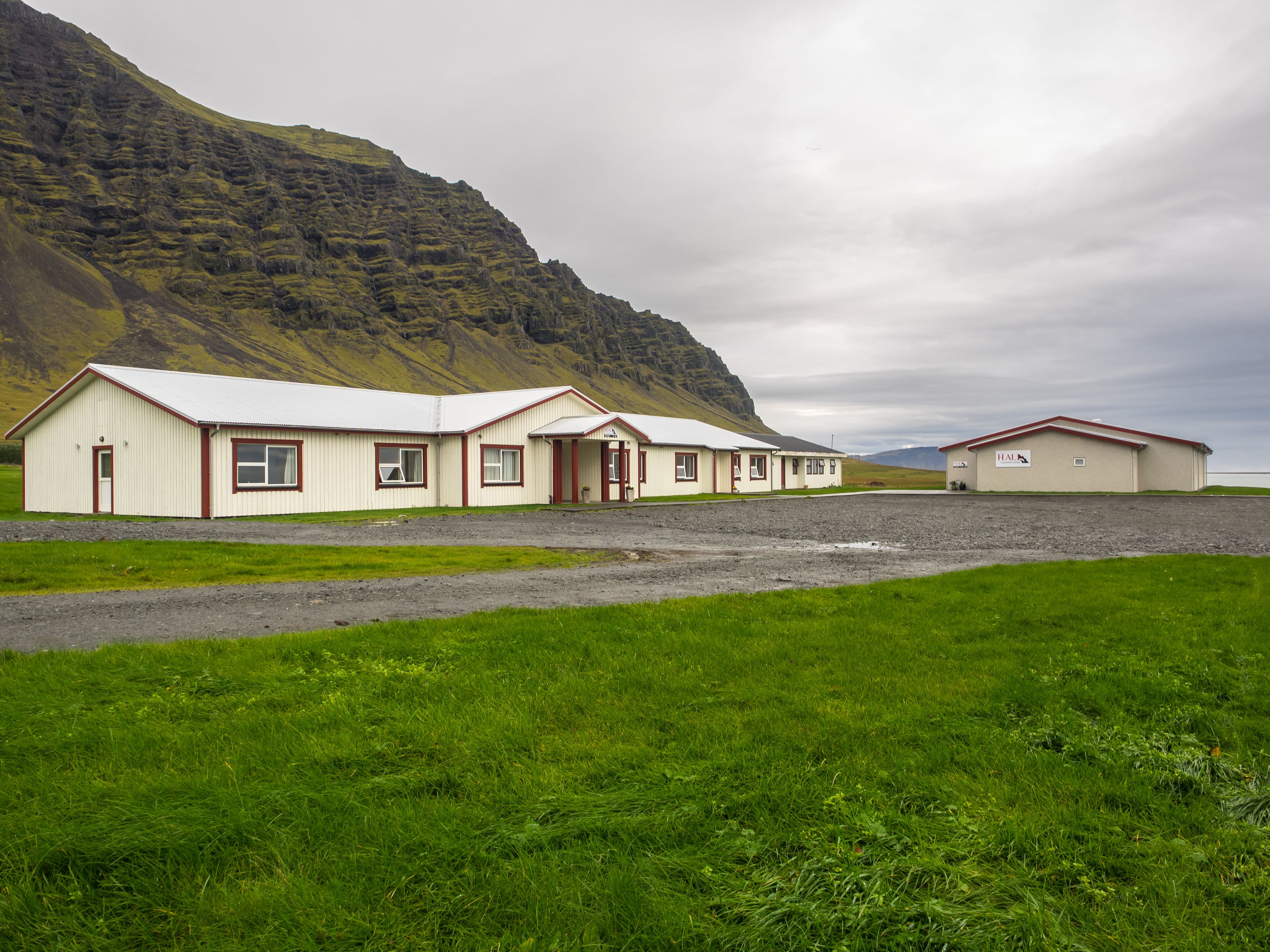 A row of two-story buildings with a flat roof, a gravel driveway, and a grassy foreground.
