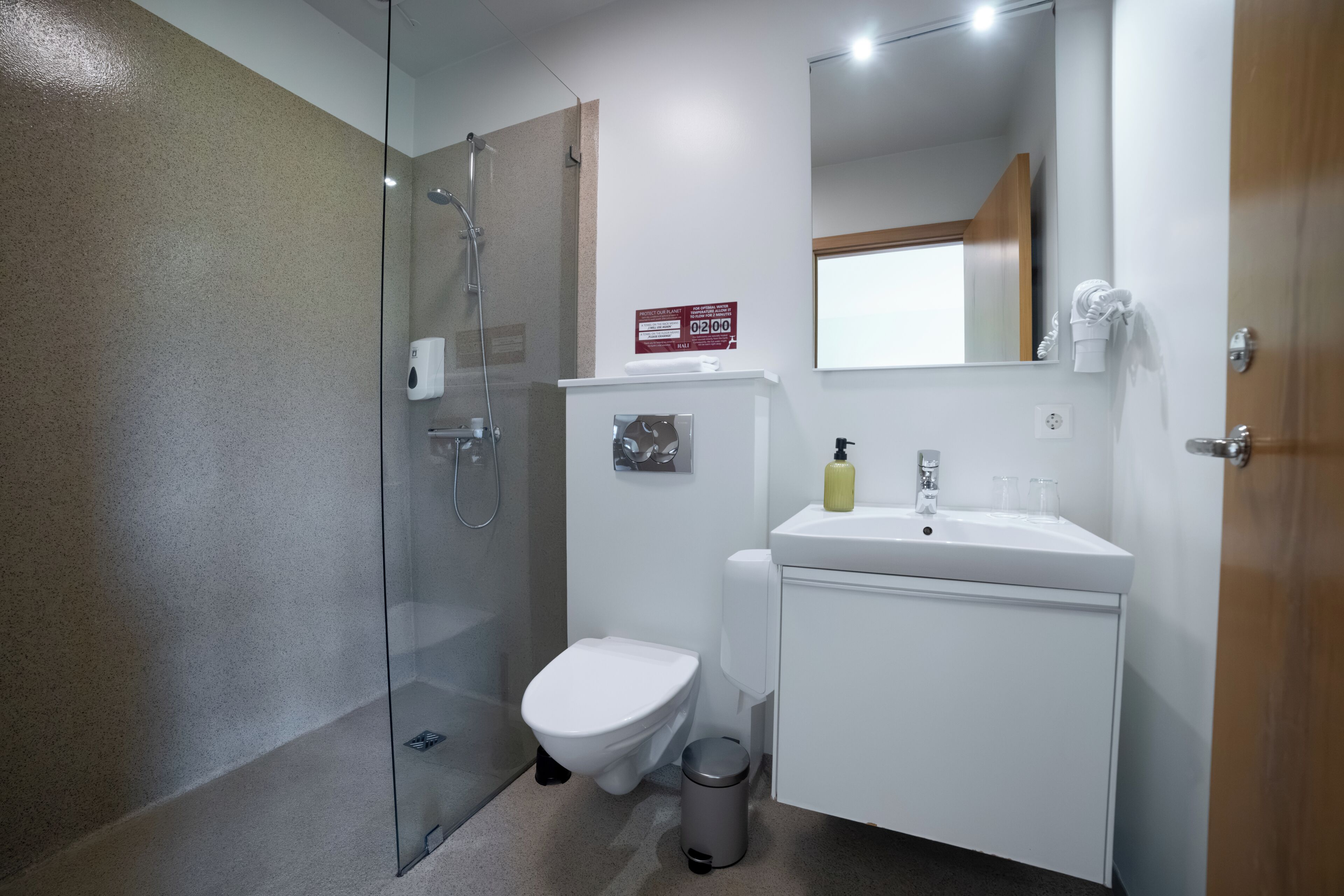A modern bathroom with a glass-enclosed shower, a toilet, a sink with a mirror, and a hand dryer.