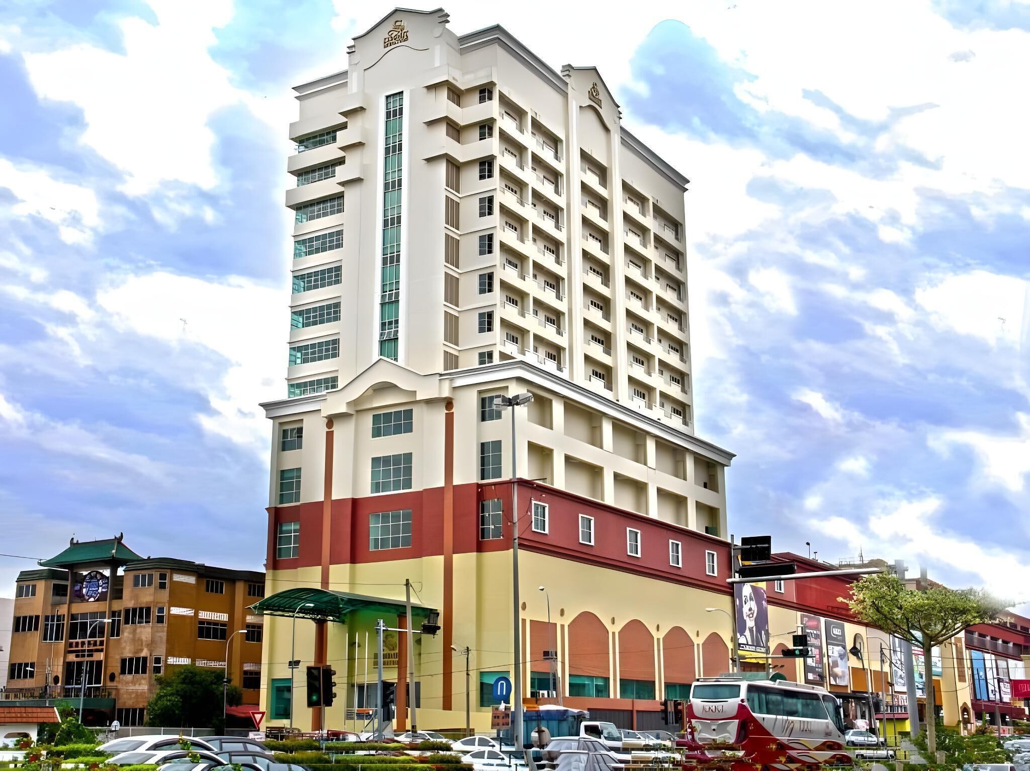 A multi-story hotel with a prominent corner entrance, a parking lot, and a street view with vehicles and other buildings.