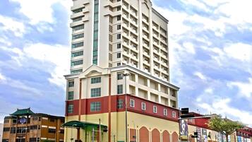 A multi-story hotel with a prominent corner entrance, a parking lot, and a street view with vehicles and other buildings.