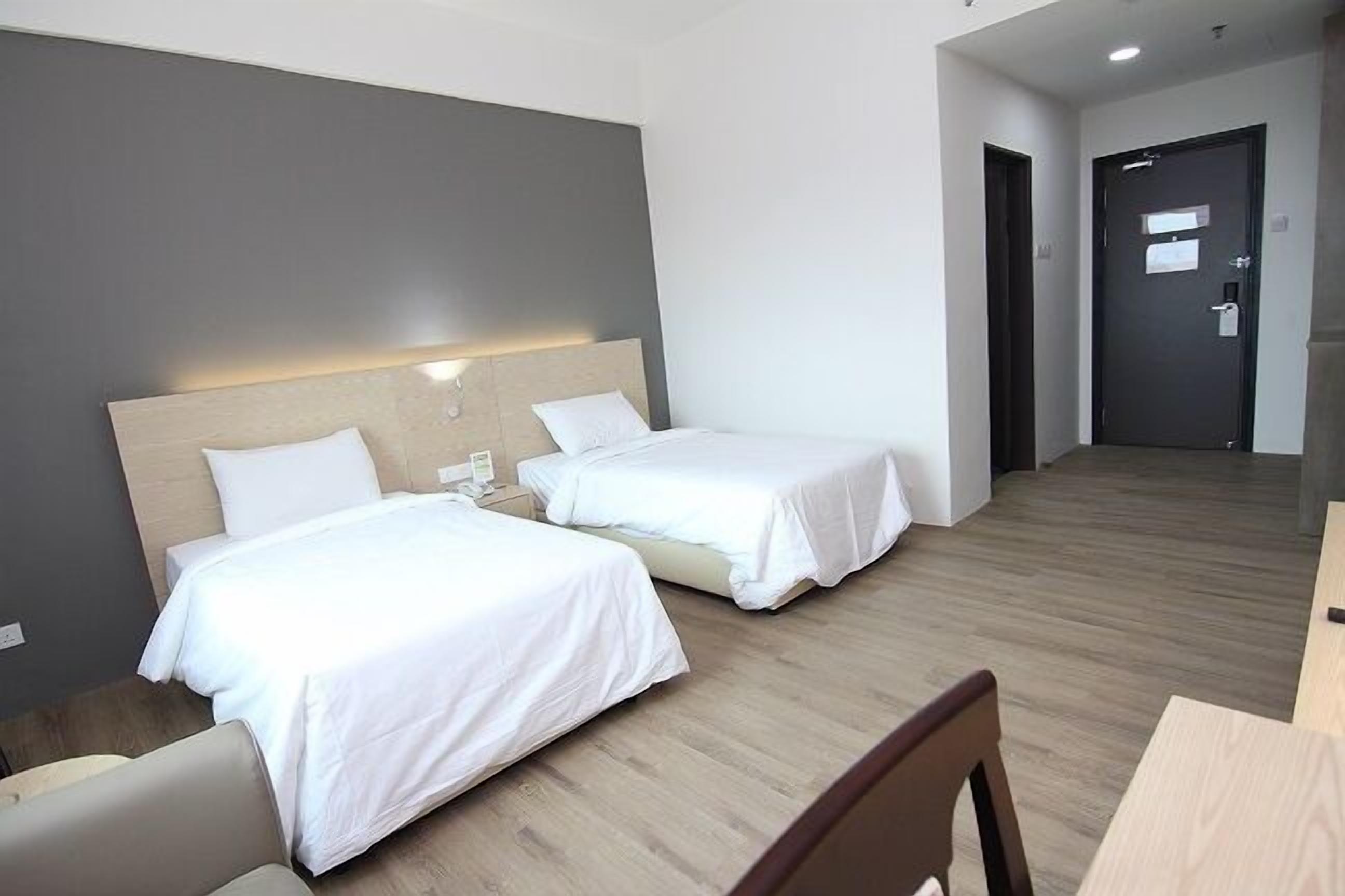 A hotel room with two beds, a wooden floor, and a desk with a chair.