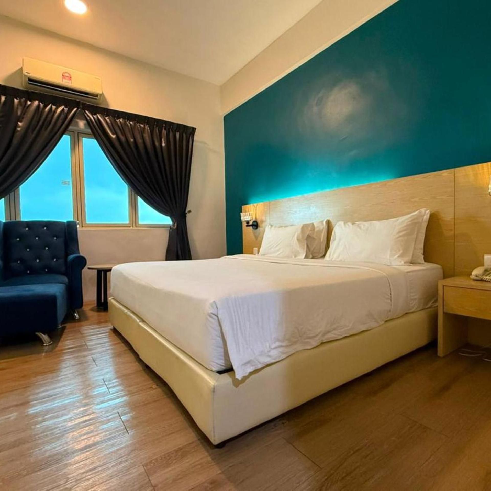 A hotel room with a large bed, a chair, a nightstand, and a window with curtains.
