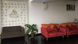 A reception area with a banner displaying 'Summit Signature Batuan', a brown sofa, a red sofa with orange cushions, and a potted plant. - Summit Signature Hotel Batu Pahat (Batu Pahat)
