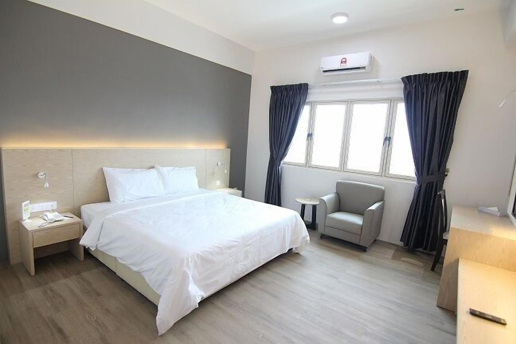 A hotel room with a bed, bedside table, chair, and window with curtains.