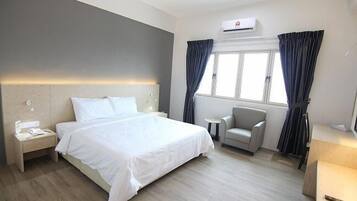 A hotel room with a bed, bedside table, chair, and window with curtains.