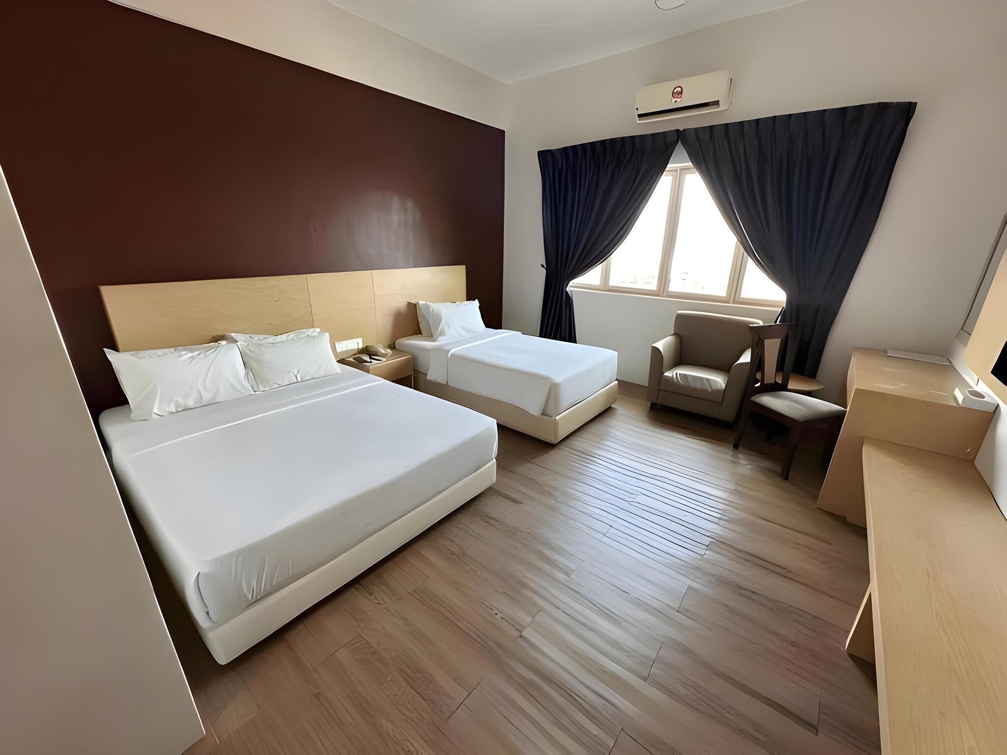 Quarto de hotel com duas camas, uma escrivaninha, uma cadeira e uma janela com cortinas.