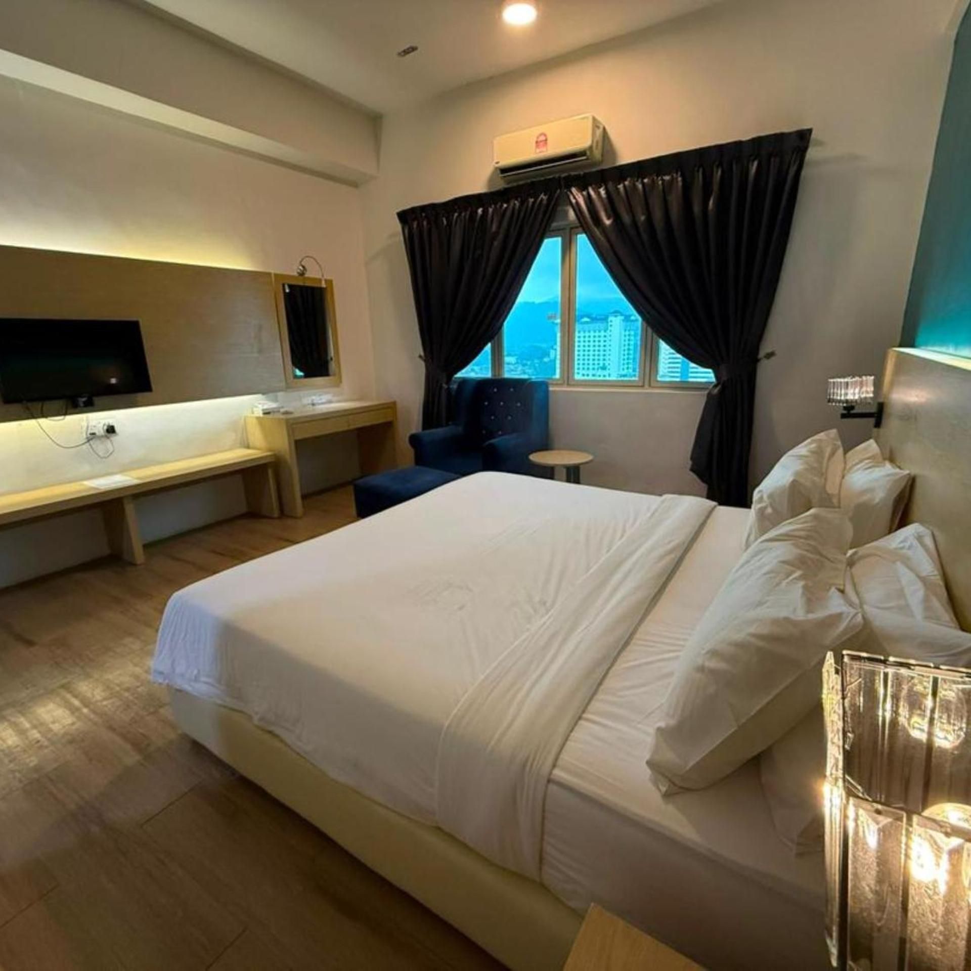 A hotel room with a large bed, a desk, a chair, a TV, and a window with curtains.