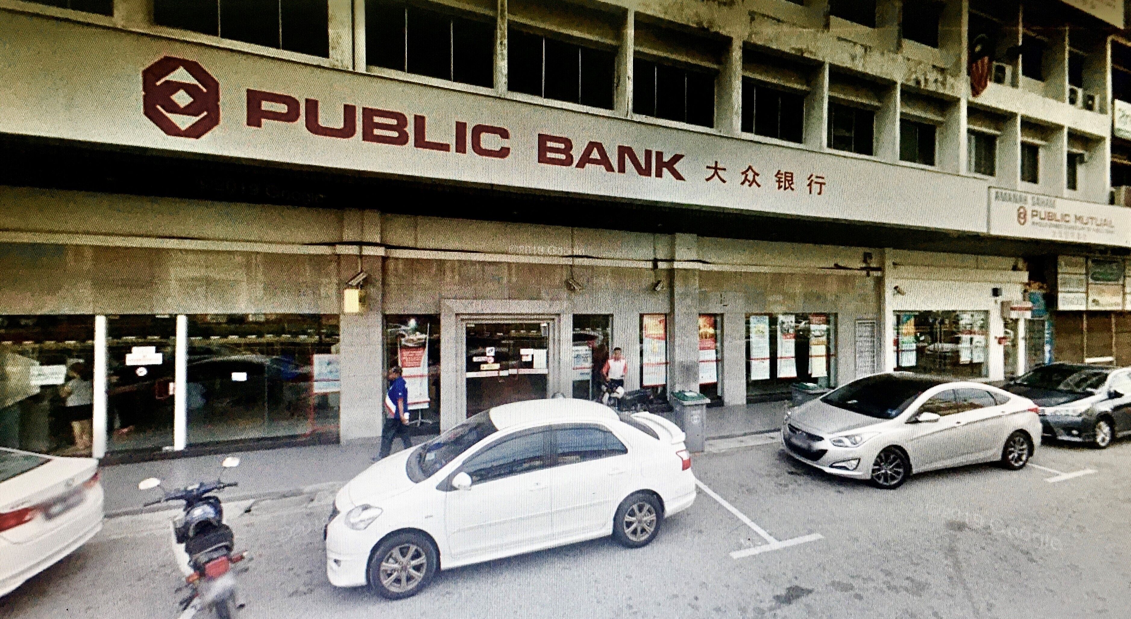 Edificio bancario público con varias entradas y coches estacionados adelante.