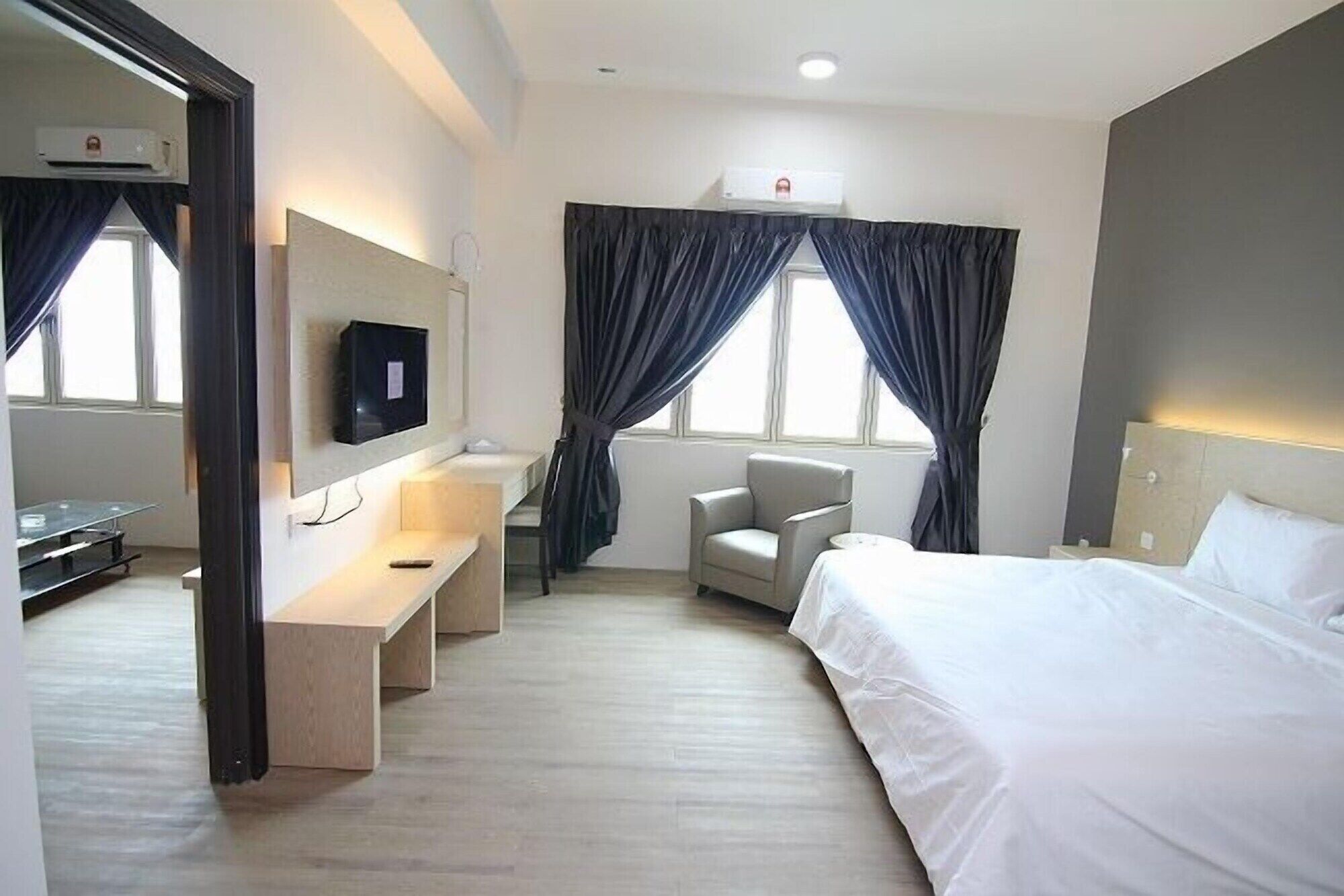 Una habitación de hotel con cama, escritorio, silla, televisión y ventana con cortinas.