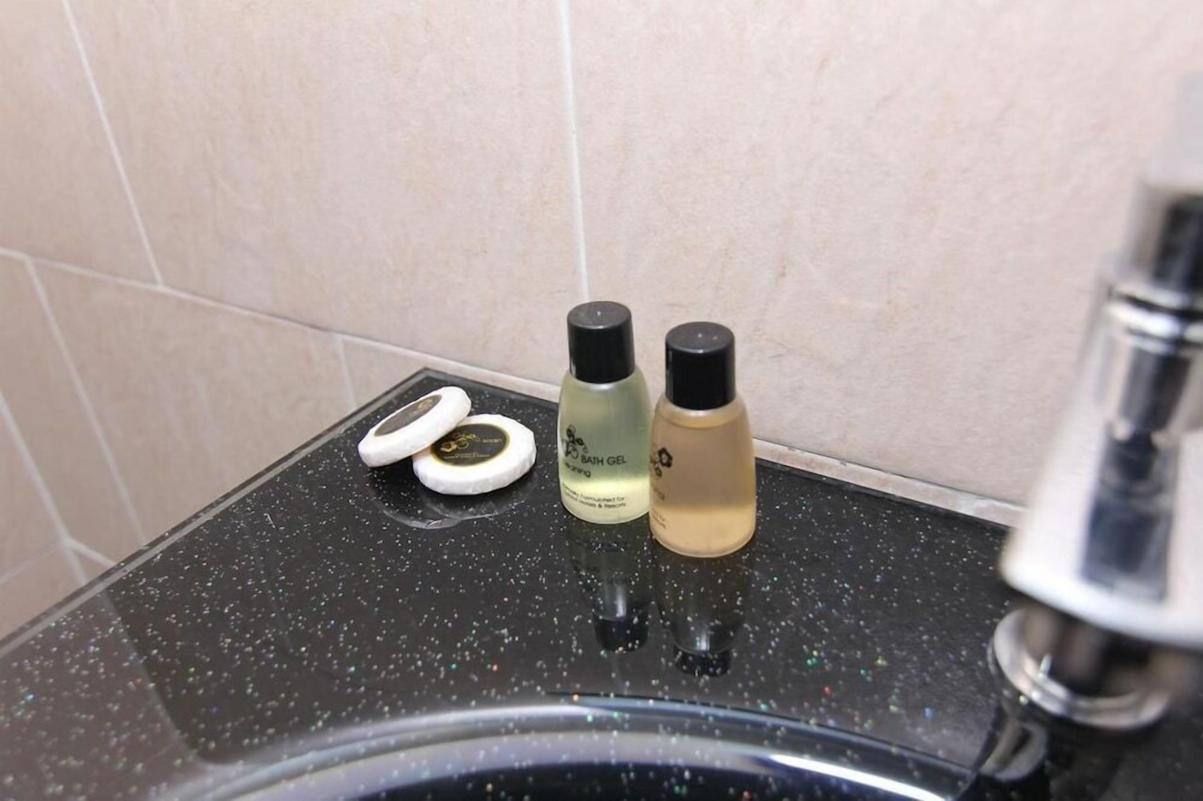 Un lavamanos de baño con encimera negra, dos botellas de gel de baño y un par de tapones para los oídos blancos.