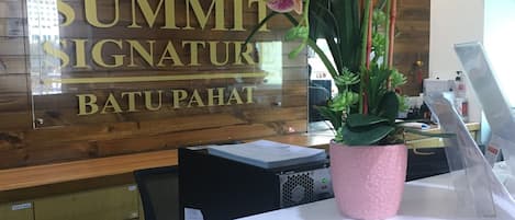 Um balcão de recepção com um painel de madeira, uma placa com a inscrição "SUMMIT SIGNATURE BATU PAHAT" e um aviso de proibição de fumar.