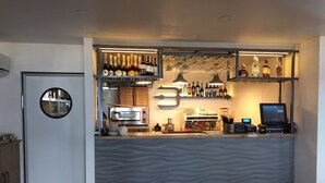 Un espace bar avec un comptoir, des étagères remplies de bouteilles et un écran numérique.
