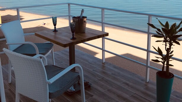 Un balcon avec une table et des chaises en bois, une plante en pot et une vue sur la mer.