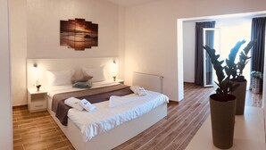 Une chambre d’hôtel moderne avec un grand lit, des tables de chevet, une œuvre d’art accrochée au mur et une vue sur l’extérieur, visible à travers l’encadrement d’une porte.