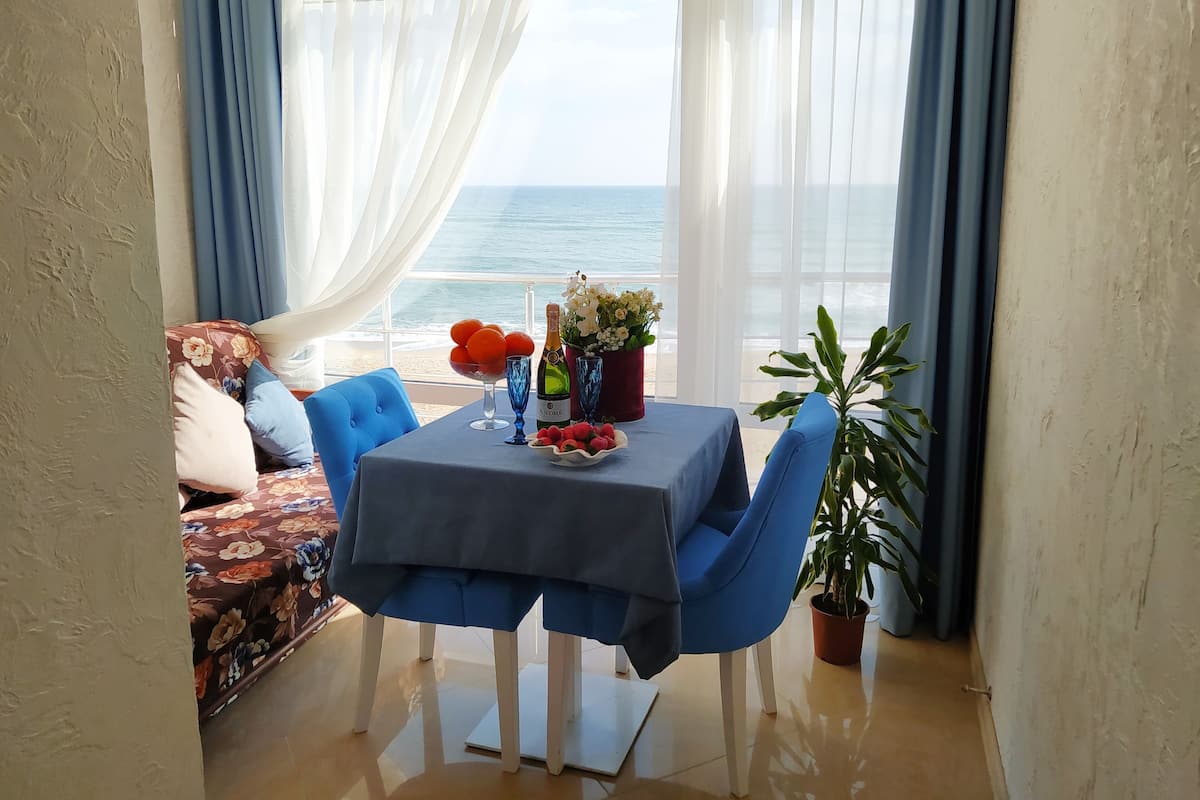 A dining area with a table set for two, a potted plant, and a view of the sea.