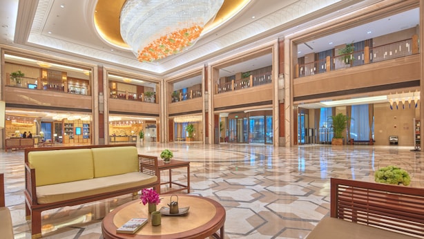 A spacious lobby with a central seating area, multiple levels, and a decorative ceiling feature. - Taishan Blossom Hotel (Tai'an)
