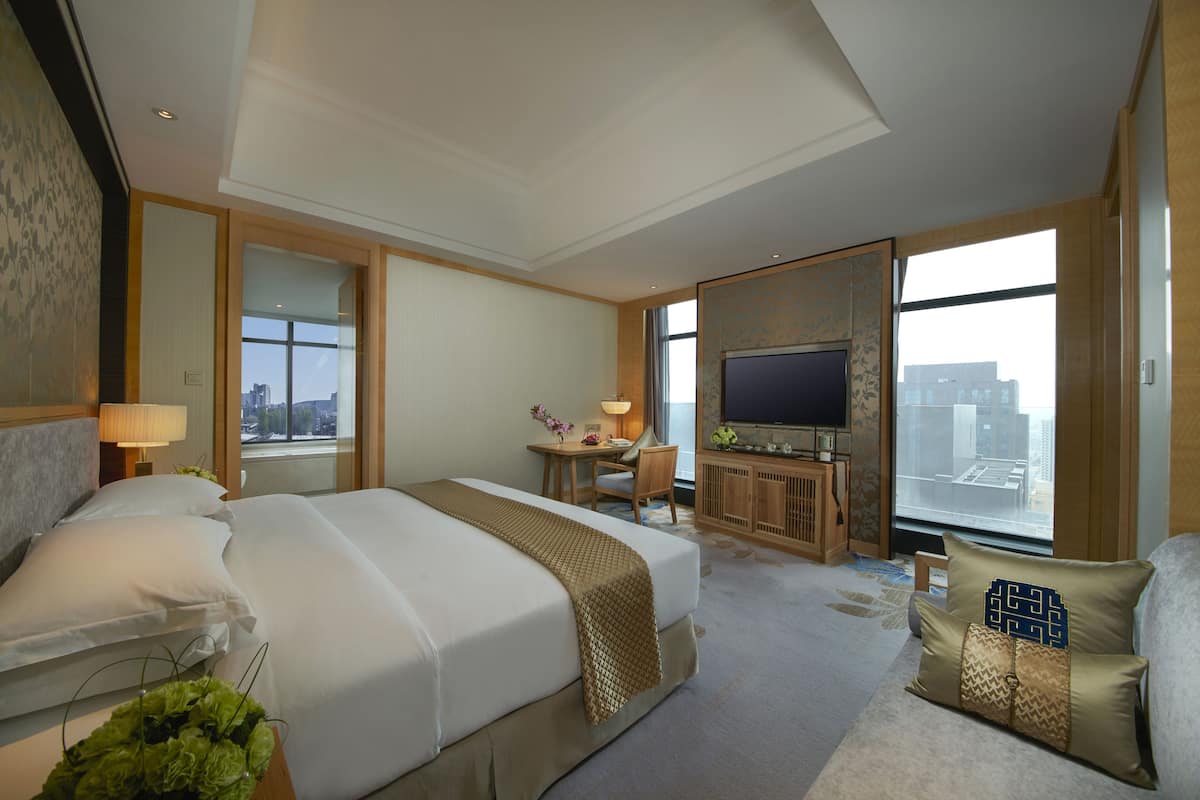 Quarto de hotel com uma cama grande, uma escrivaninha, uma televisão e vista para a cidade.