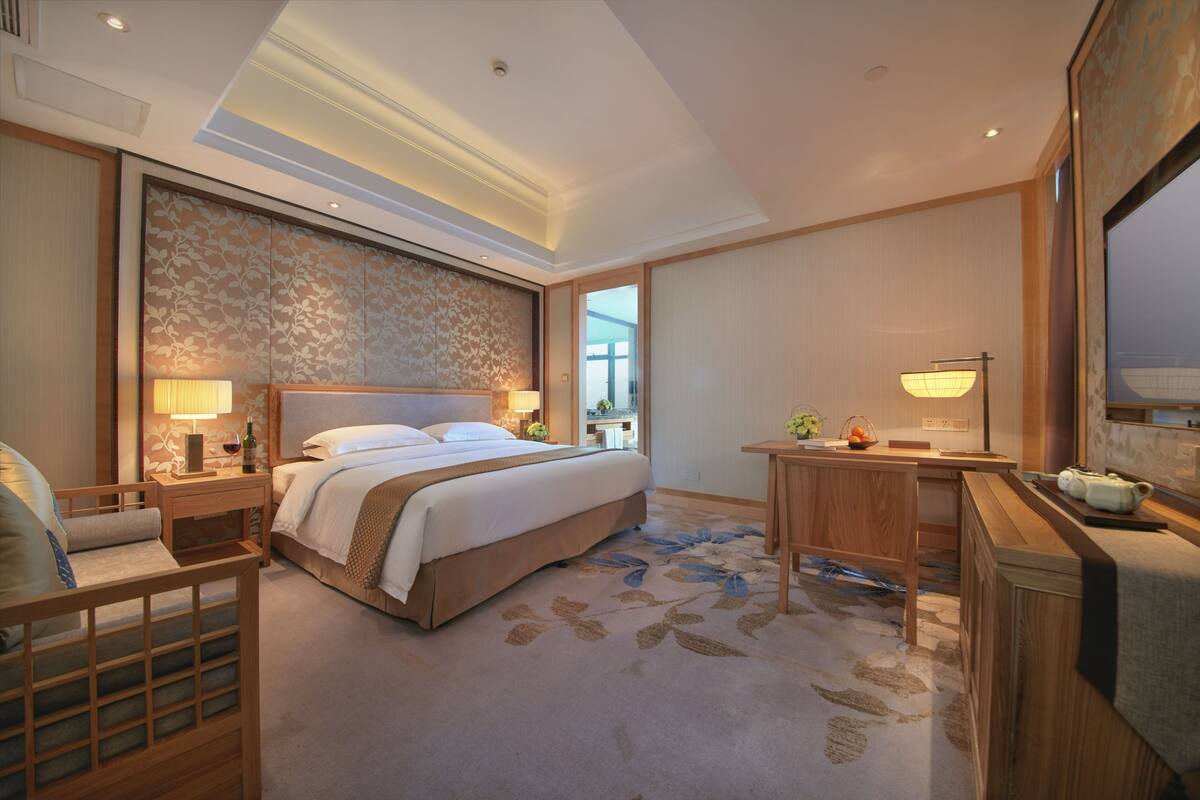 Quarto de hotel moderno com cama grande, mesas de cabeceira, escrivaninha e uma cadeira.