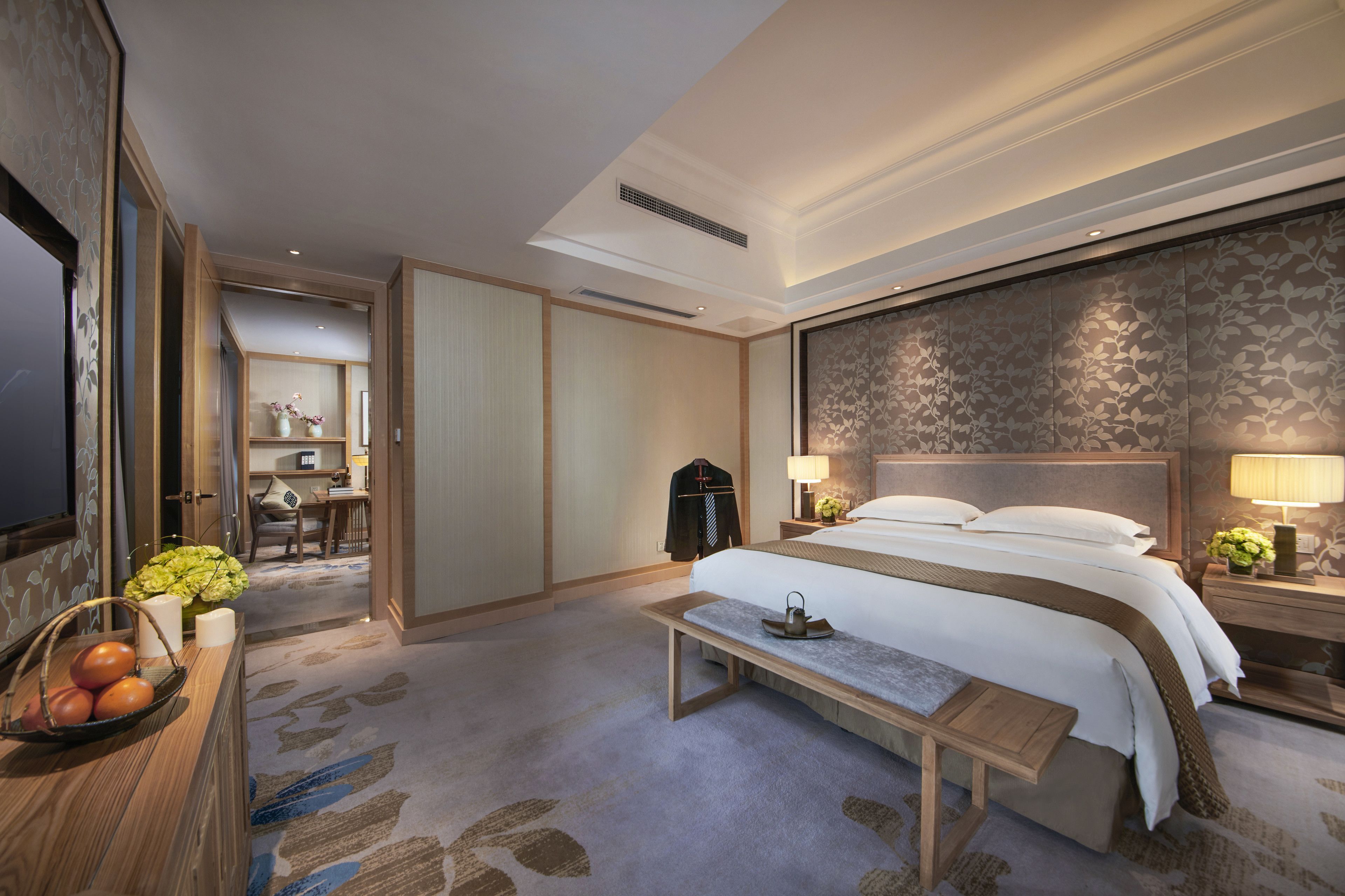 A hotel room with a large bed, bedside tables, a desk, and a seating area.