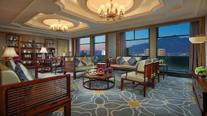 A spacious living area with a high ceiling, chandeliers, a large window with a city view, and a patterned carpet. - Taishan Blossom Hotel (Tai'an)
