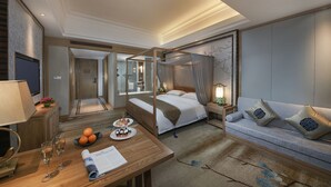 A hotel room with a four-poster bed, a sofa, a desk with a lamp, and a small table with oranges and a plate of food. - Taishan Blossom Hotel (Tai'an)