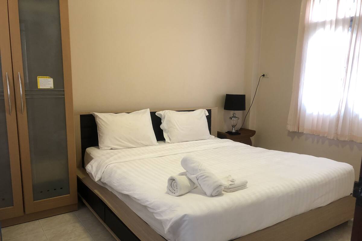 Un lit bien fait, avec des draps blancs et des serviettes pliées, une lampe de chevet et une fenêtre avec des rideaux.