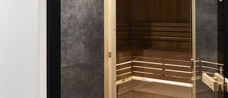 Una sauna moderna con recinto de vidrio, bancos de madera y un banco con toallas.
