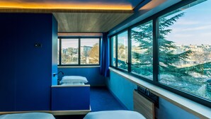 A modern hotel room with two beds, a small bathroom, and a large window offering a city view. - Yooma Urban Lodge Tour Eiffel (Paris)
