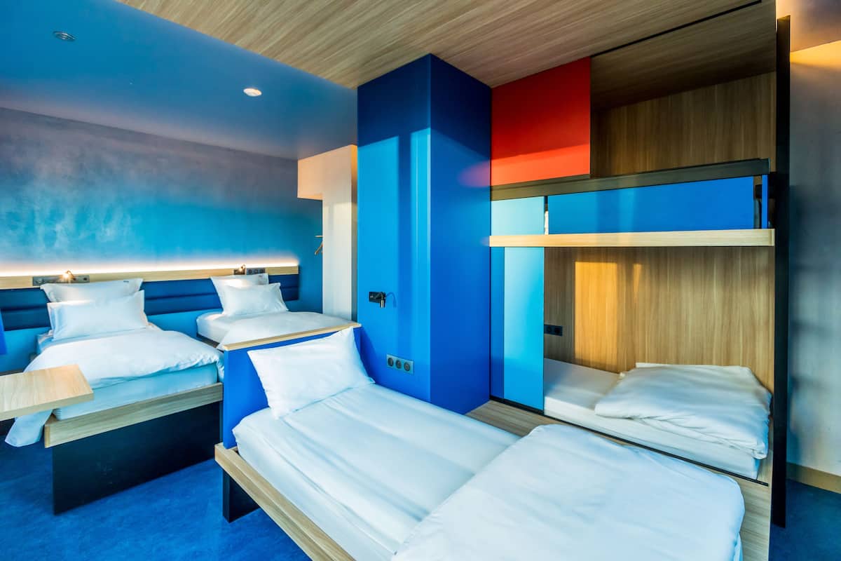 Ein modernes Hotelzimmer mit Stockbetten, einem Schreibtisch und einer blauen Akzentwand.
