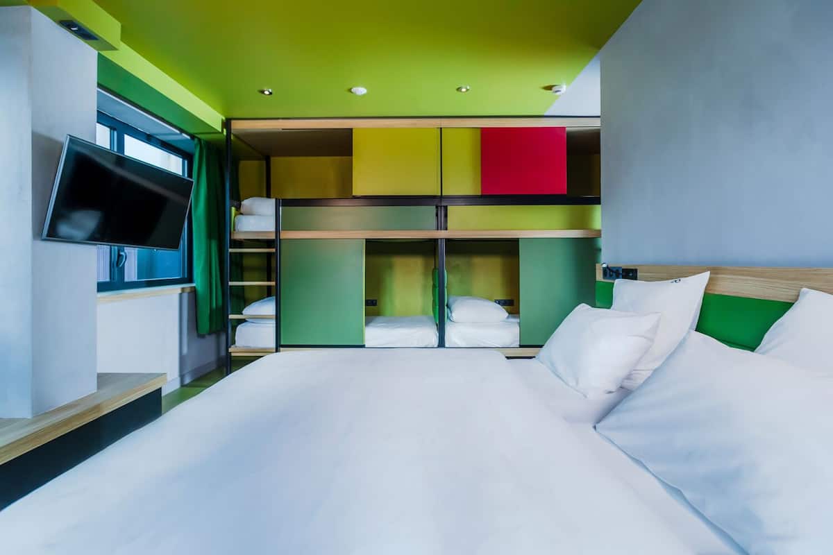 Ein Hotelzimmer mit einem Bett, einem Fernseher, einem Kleiderschrank und einer grünen Decke.