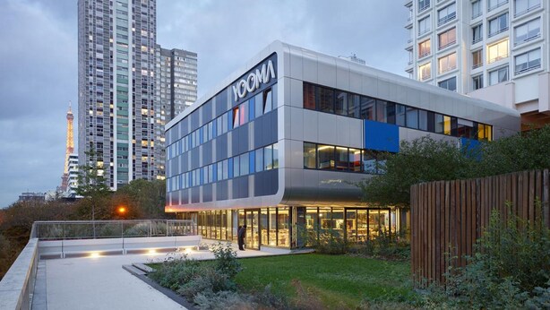A modern building with the name "YOOMA" on the facade, surrounded by greenery and a pathway. - Yooma Urban Lodge Tour Eiffel (Paris)