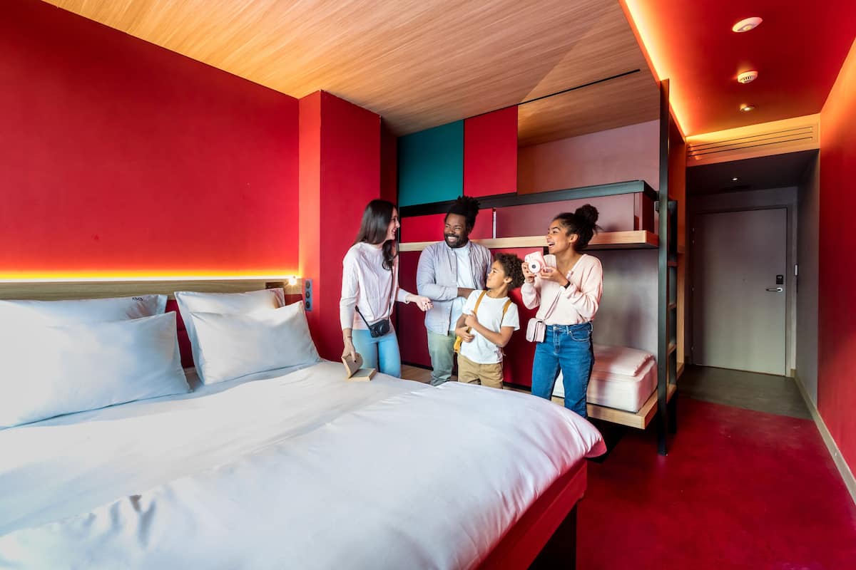 Ein Hotelzimmer mit einem großen Bett, einem Etagenbett und einer roten Akzentwand.
