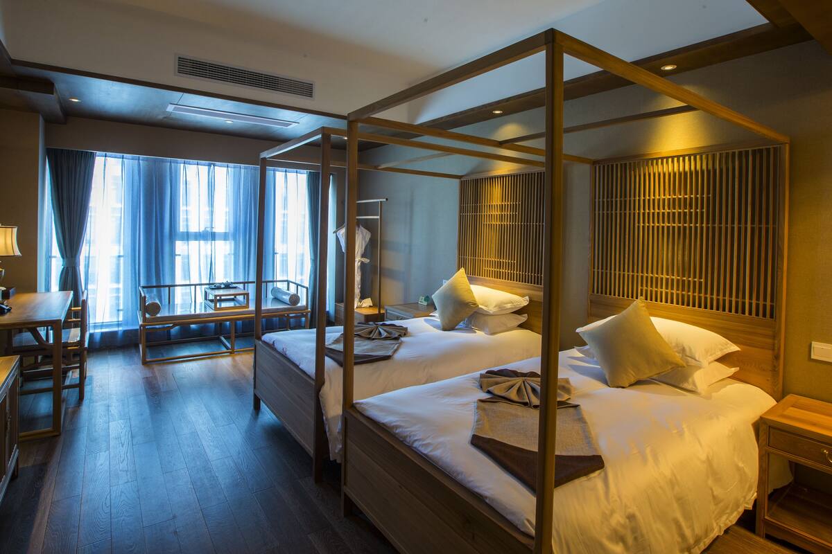 A four-poster bed with a wooden frame, a desk with a lamp, and a chair in a hotel room.