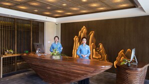 A reception desk with two staff members, a wooden reception desk, a computer, and a decorative wall. - Blossom  Tao Hotel （Hangzhou Olympic Center） (Hangzhou)