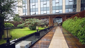 A pathway leading to a building with a modern design, a water feature, and well-maintained greenery. - Blossom  Tao Hotel （Hangzhou Olympic Center） (Hangzhou)