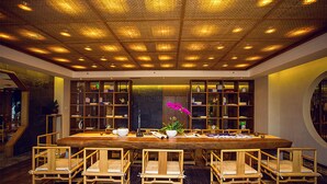 A spacious room with a large wooden table surrounded by chairs, a ceiling with a grid pattern, and bookshelves along the walls. - Blossom  Tao Hotel （Hangzhou Olympic Center） (Hangzhou)