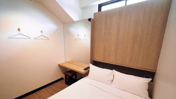 A bedroom with a bed, a wooden headboard, a bedside table, and two wall-mounted light fixtures. - T Hostel at Victory Monument (Bangkok)