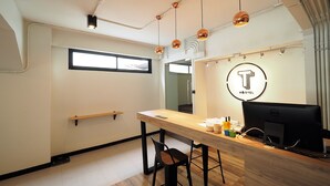 A modern office space with a wooden desk, a computer, and a chair. There is a window and a wall-mounted sign with a letter 'T'. - T Hostel at Victory Monument (Bangkok)