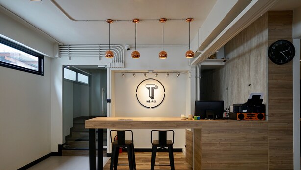 A modern hostel interior with a central bar area, two bar stools, a visible staircase, and a clock on the wall. - T Hostel at Victory Monument (Bangkok)
