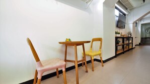 A hallway with two wooden chairs and a small table, a black shelf with plants, and a staircase in the background. - T Hostel at Victory Monument (Bangkok)