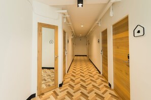 A hallway with wooden flooring, white walls, and doors with black signage. - T Hostel at Victory Monument (Bangkok)