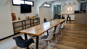 A modern hotel lobby with a long wooden reception desk, multiple seating areas, and a TV mounted on the wall. - T Hostel at Victory Monument (Bangkok)